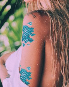 Woman wearing blue mermaid scale temporary tattoos.
