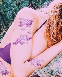 Woman on the rocks with mermaid scale temporary tattoos.