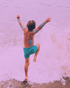 Boy jumping into waves while wearing mermaid scale temporary tattoos.