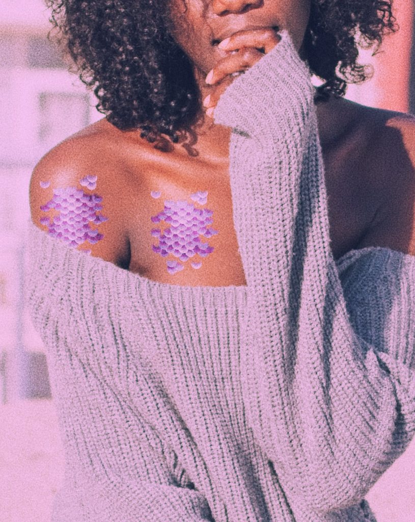 Woman in a sweater on the beach wearing purple mermaid scale temporary tattoos.